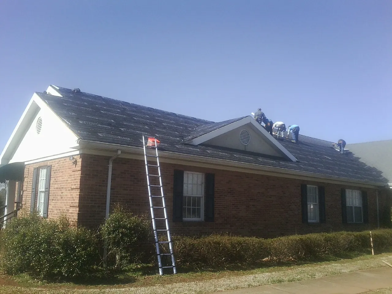 Crew tearing shingles off a brick ranch roof with a ladder set — Metal Roof Repair work by our crew in Allensville