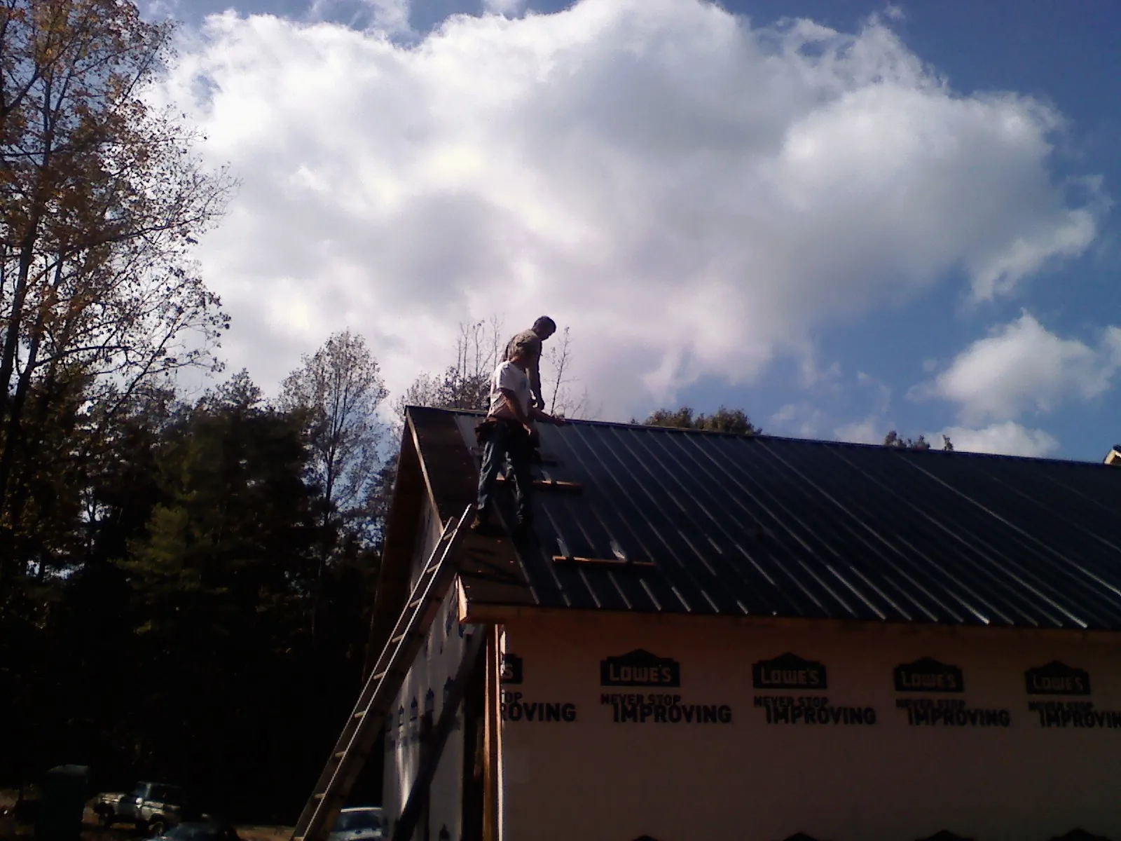 Roofer fastening dark metal panels high against a cloudy sky, from a Roof Inspection job in Allensville